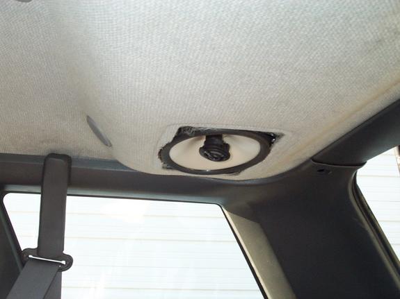 Headliner cutout above rear pillar with mounted speaker and seatbelt visible