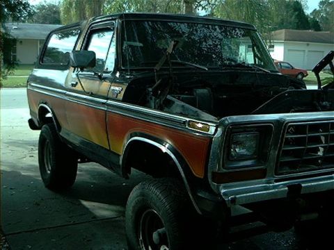 1979 Ford Bronco - This 1979 Ford Bronco features a distinctive orange and black paint scheme and its hood is open, revealing the engine bay.