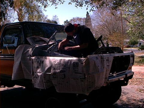 1979 Ford Bronco - A man works on the engine of a 1979 Ford Bronco, with the front end covered in newspaper.
