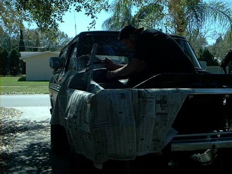 1979 Ford Bronco - A man works on the engine bay of a 1979 Ford Bronco, with the front grille covered in newspaper.