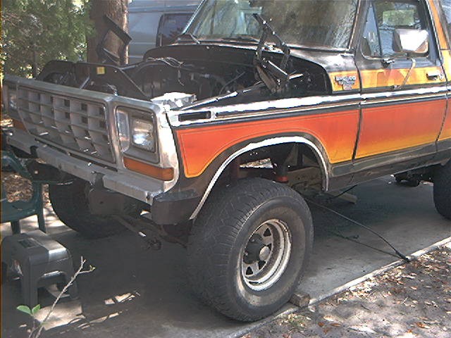 Front end of a 1978 Ford Bronco with hood open, showing orange and yellow side stripes