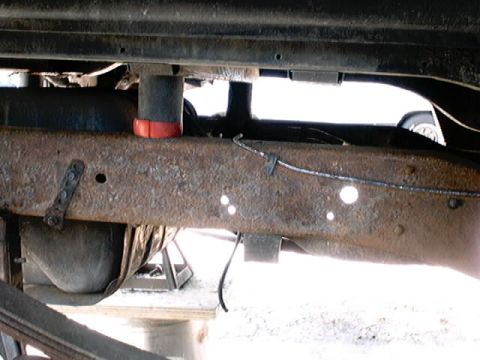 1979 Ford Bronco - Undercarriage view of a heavily rusted vehicle frame, showing a fuel tank and suspension parts.