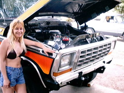 1979 Ford Bronco - Woman poses with a 1978 Ford Bronco, hood up, showing the engine bay. Another vehicle is parked behind.