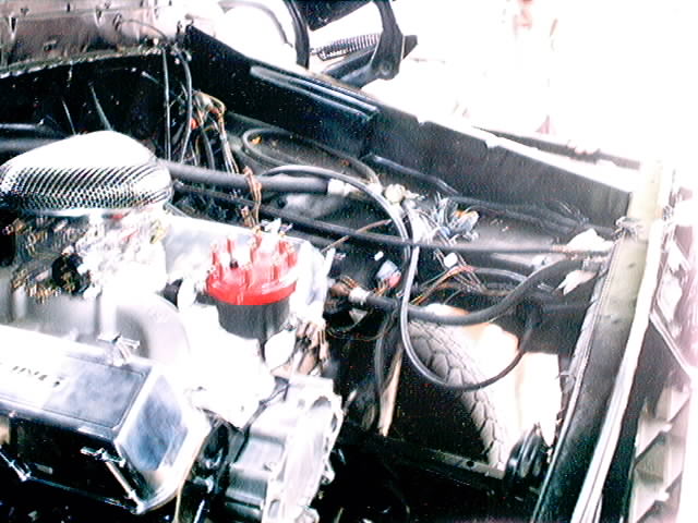 Engine bay with V8 engine, carburetor, and distributor. Wires and hoses are visible