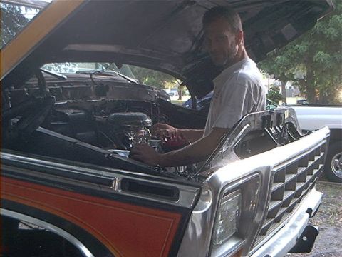 1979 Ford Bronco - A man is shown working on the engine of a classic Ford truck, with another vehicle parked nearby.