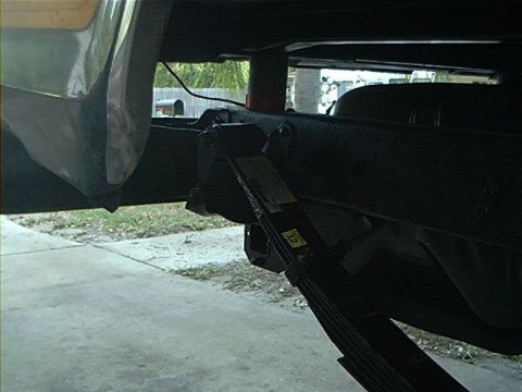 1979 Ford Bronco - A jack is positioned under the leaf spring of a vehicle's undercarriage, revealing a yellow sticker with the number 12.
