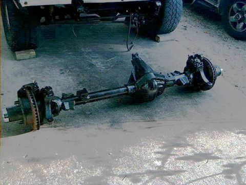 1979 Ford Bronco - A vehicle's front axle assembly sits on the ground, detached from the chassis.