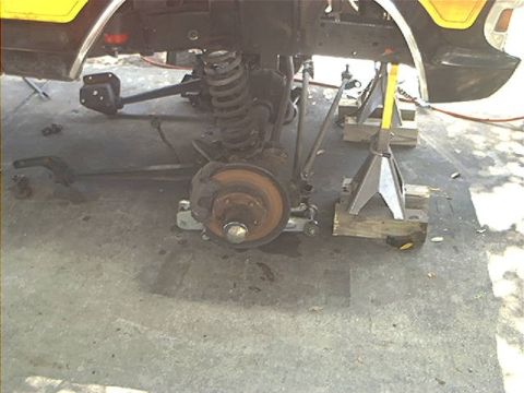 1979 Ford Bronco - The front suspension and wheel assembly of a yellow 1979 Ford Bronco are visible while the vehicle is supported by jack stands.