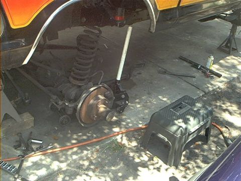 1979 Ford Bronco - The rear suspension and axle of a vehicle are visible, undergoing maintenance with tools scattered around.
