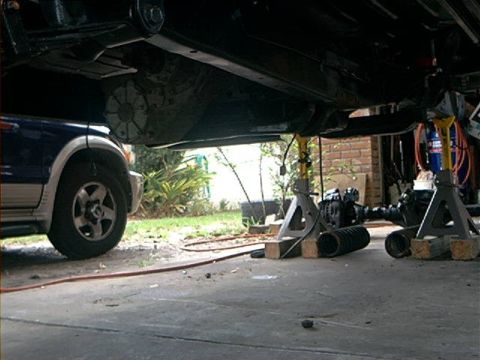 1979 Ford Bronco - The underside of a vehicle is visible, supported by jack stands, with parts of the drivetrain removed.