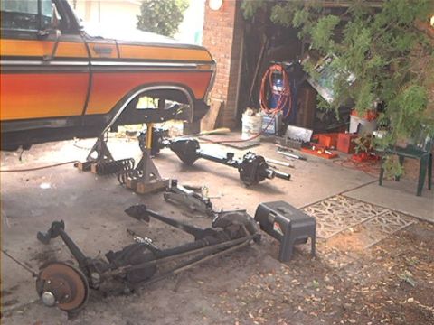 1979 Ford Bronco - A Ford truck's body is elevated on jack stands, with its axles disassembled and laid out on the garage floor.
