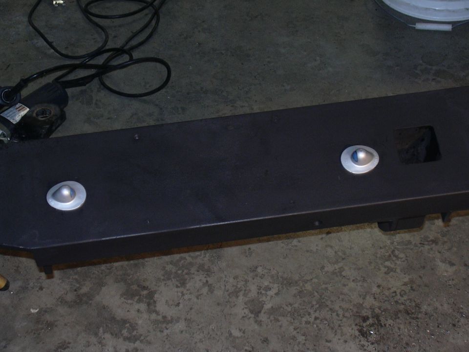 Black metal bumper part with two circular silver reflectors and a square cutout