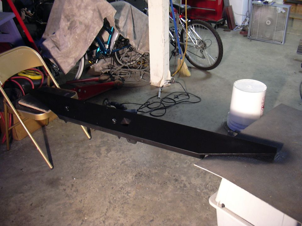 Long black fabricated steel bumper or rocker bar lying across a cluttered garage floor