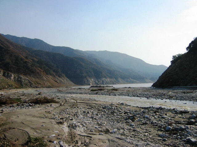 Rocky riverbed winding between hazy forested mountains
