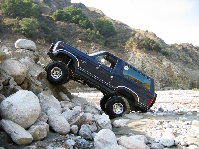 Dark blue lifted Ford Bronco climbing boulders in a rocky creek bed