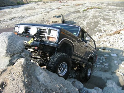 1985 Ford Bronco - This modified Ford Bronco is tackling a challenging off-road course with a second vehicle in the background.