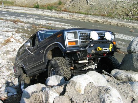 1985 Ford Bronco - A black Ford Bronco navigates a rocky terrain near a stream.