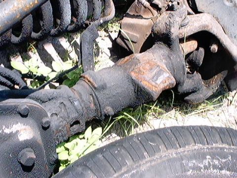 1979 Ford Bronco - Close-up of heavily corroded vehicle suspension components and a tire lying on grass.