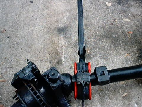 1979 Ford Bronco - Close-up view of a black steering linkage assembly with red bushings, resting on a concrete surface.