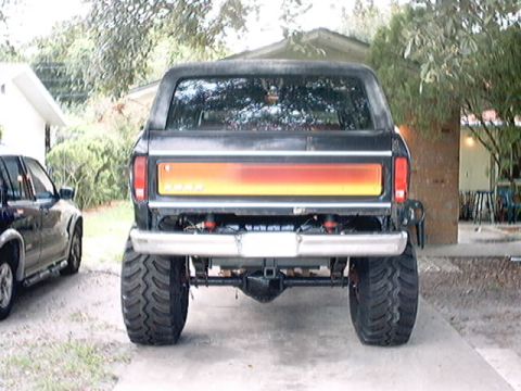 1979 Ford Bronco - Rear view of a lifted black Ford Bronco with custom taillight trim and oversized tires.