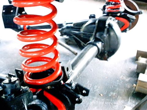 1979 Ford Bronco - Close-up view of vehicle suspension parts, including a red coil spring and differential assembly.