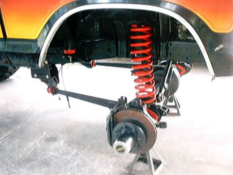 1979 Ford Bronco - Close-up view of the front suspension and wheel assembly, bright red coil springs and disc brakes.