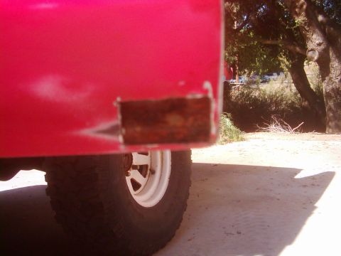 1978 Ford Bronco - Close-up of a red vehicle's body panel showing rust, with a tire and wheel in the foreground.