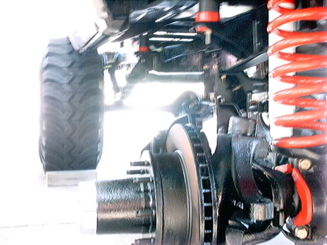 close-up of a vehicle's front suspension, showing a large tire, brake rotor, and red coil spring