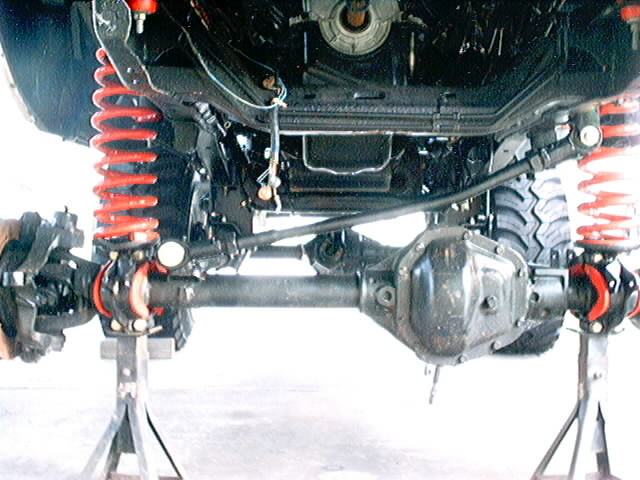 Underside of a vehicle on jack stands, showing the front axle, differential, and red coil springs