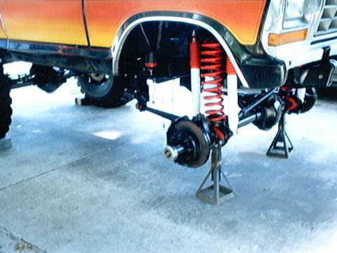 1979 Ford Bronco - The front suspension of an orange and yellow Ford Bronco is visible, supported by jack stands.