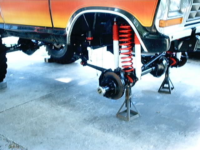 Orange and yellow Ford Bronco front suspension on jack stands, showing red shocks and springs