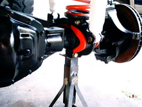 1979 Ford Bronco - Close-up of a vehicle's rear axle assembly, a red coil spring and white shock absorber, resting on jack stands.