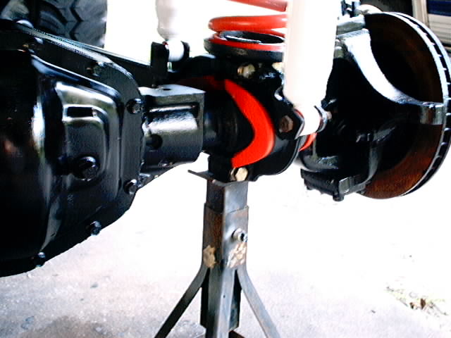 Rear axle assembly with red coil spring and white shock absorber, supported by jack stands