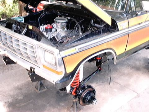 1979 Ford Bronco - Front end of a 1979 Ford Bronco undergoing repairs, with the hood up and suspension components removed.