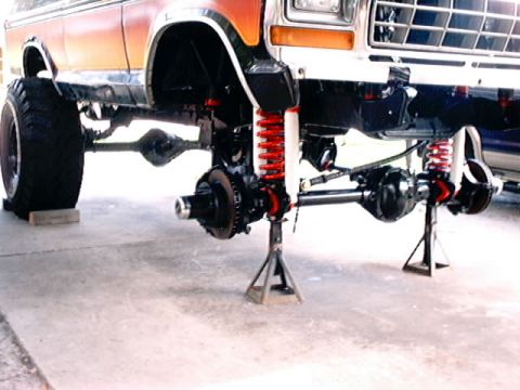 1979 Ford Bronco - The front suspension and axles of a lifted Ford Bronco are visible, with the vehicle supported by jack stands.