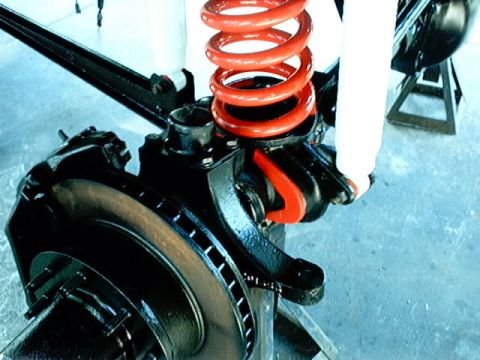 1979 Ford Bronco - Close-up of a vehicle's front suspension components, including a red coil spring and shock absorber.