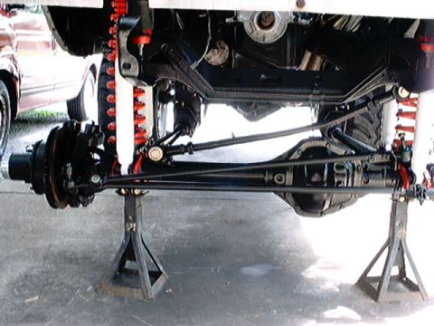 1979 Ford Bronco - The underside of a vehicle is shown, supported by jack stands, revealing its suspension and drivetrain.