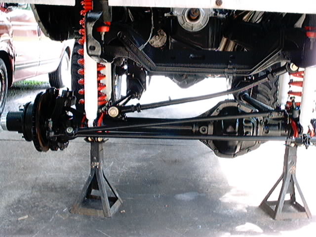 Undercarriage of a vehicle on jack stands, showing suspension and drivetrain components