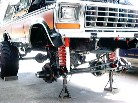 1979 Ford Bronco - Front suspension and chassis of a Ford Bronco undergoing modifications, lifted on jack stands.