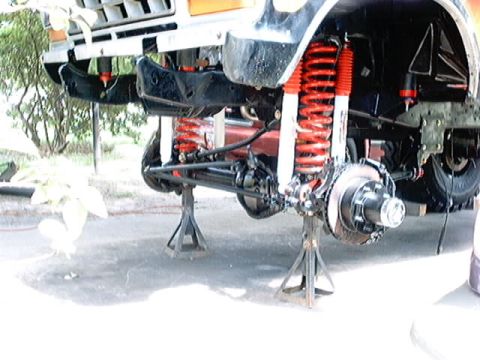 1979 Ford Bronco - Front suspension of a 1979 Ford Bronco, lifted on jack stands, showing red shocks and springs.