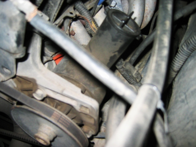 Engine bay close-up with cylindrical filter, hoses, metal pipe and drive belt pulley