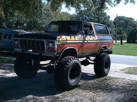 1979 Ford Bronco - This lifted 1979 Ford Bronco features a distinctive orange and yellow stripe pattern and is equipped with large off-road tires.
