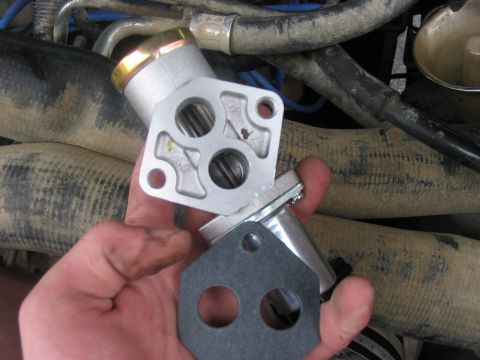 1988 Ford Bronco - A hand holds a metal engine part and gasket, with hoses and engine components visible in the background.
