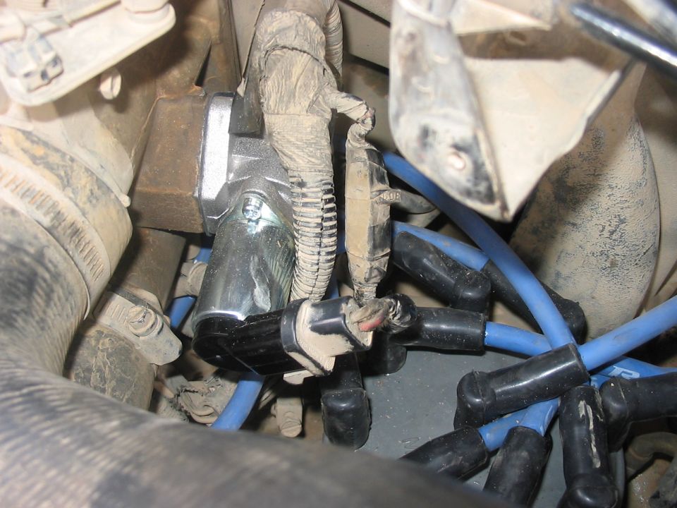 Engine bay with blue spark plug wires and a silver sensor