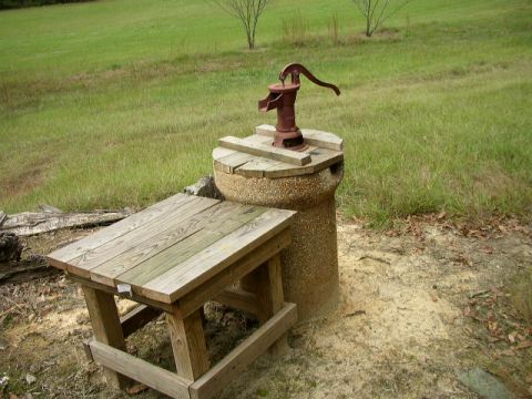 1995 Ford Bronco - A rustic scene an old hand water pump and a wooden table set in a grassy outdoor area.