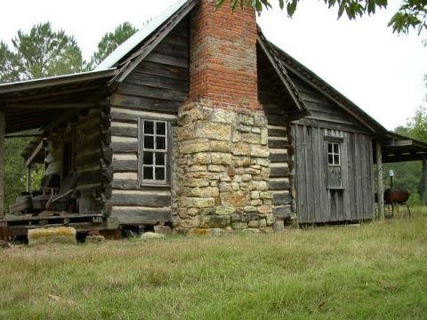 1995 Ford Bronco - Exterior view of a rustic log cabin a prominent stone chimney and weathered wooden walls.