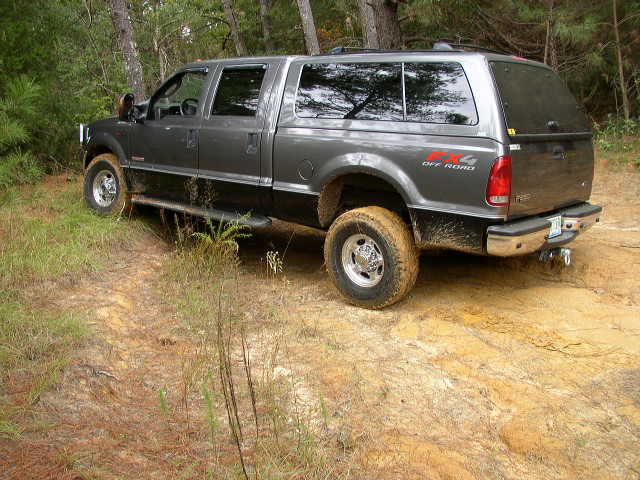 Gray Ford Excursion SUV with black lower body trim driving on a dirt trail