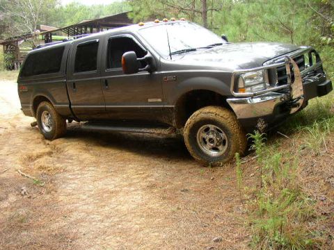 1995 Ford Bronco - A dark gray Ford Excursion SUV with a cap is shown driving on a dirt path in a wooded area.