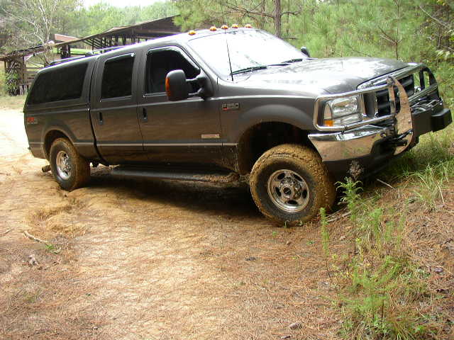 Dark gray Ford Excursion SUV with a cap on the bed, driving on a dirt road