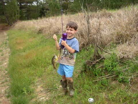 1995 Ford Bronco - A young boy proudly displays his catch while fishing in a grassy, wooded area.